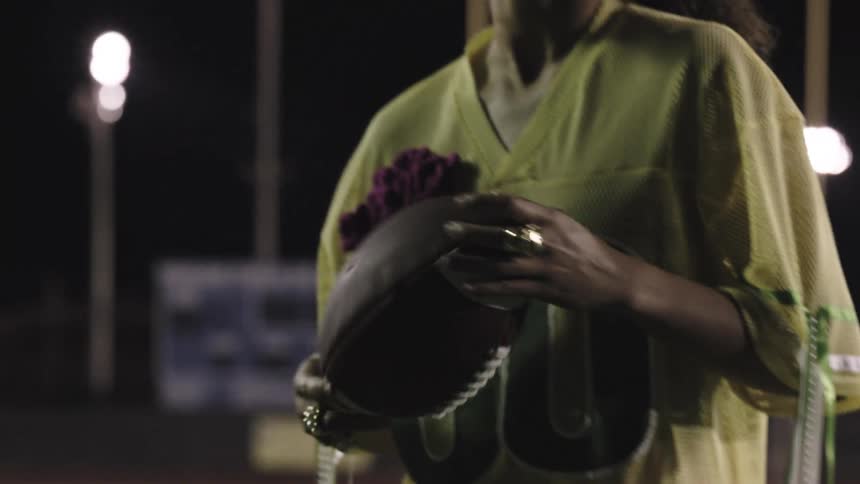 Female athlete is holding a football outdoors during the night