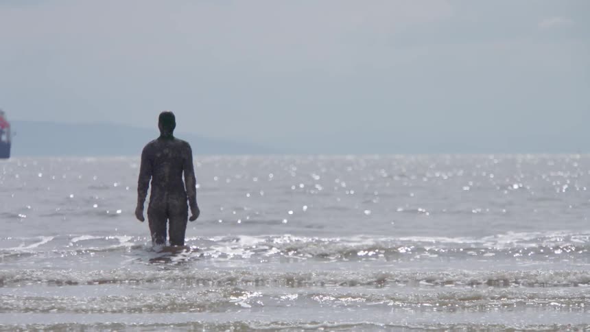 Statue of standing person in shallow ocean water