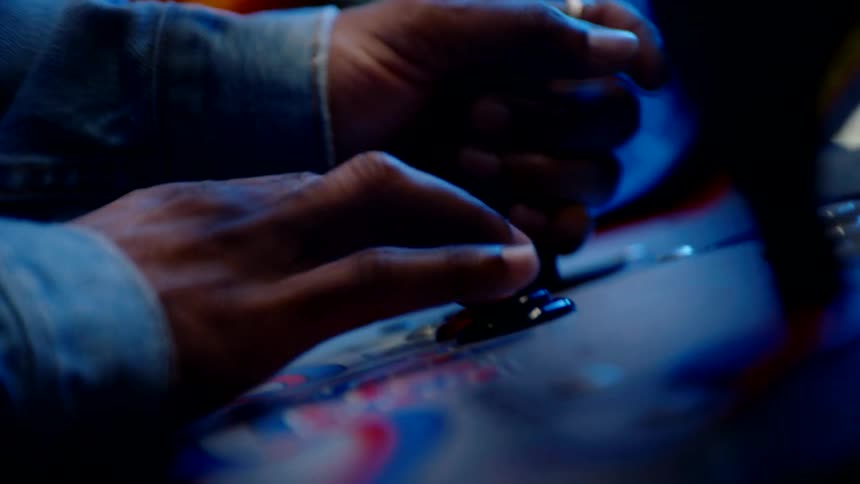 A black persons arm is seen aggressively playing an arcade game