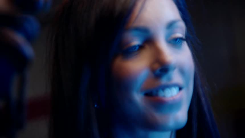 The face of a young woman who is smiling while looking straight ahead and her face is being illuminated by a blue light