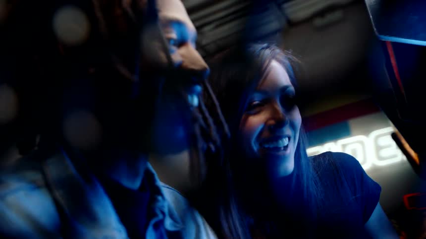 Two people stand in a neonlit arcade smiling while playing