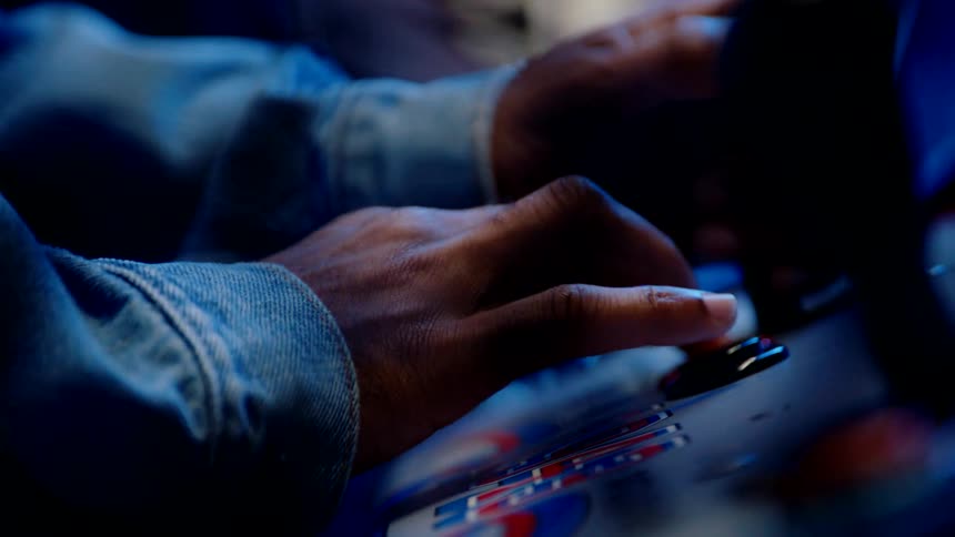 A persons hands using their fingers to quickly press a red button on a control desk