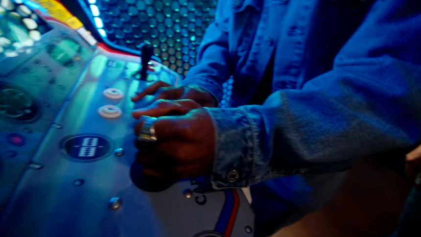 A man is playing a video game while the woman watches in the arcade