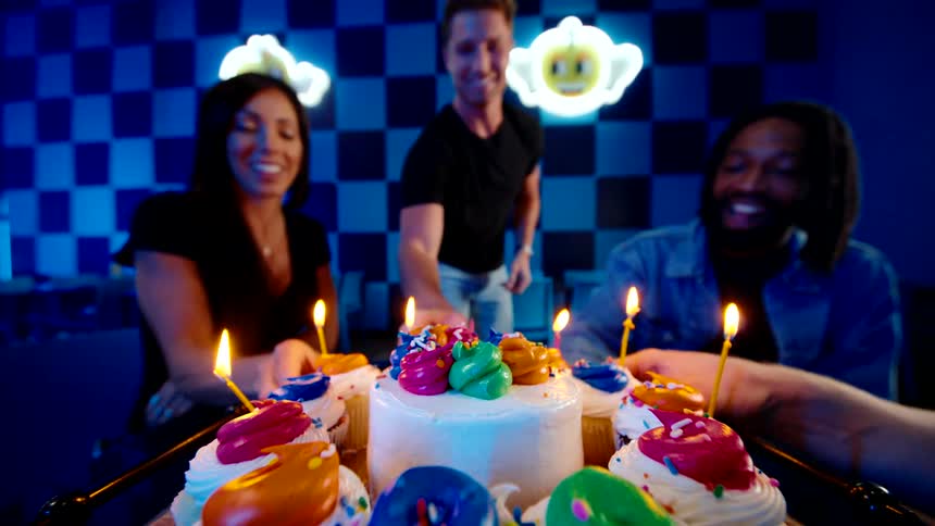 Friends cheer with cupcakes around a vibrant birthday cake in a colorful party setting