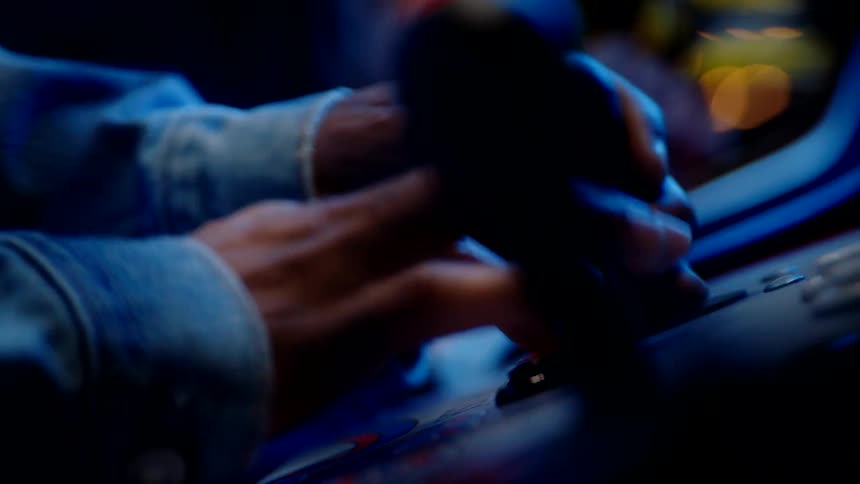 An arcade gamer wearing a jean jacket plays passionately at night