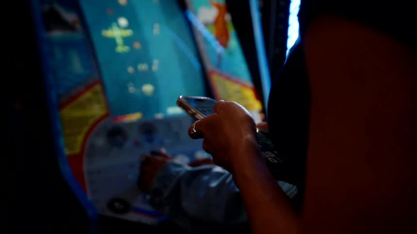 A woman scrolls through her phone while standing beside a man playing an arcade game in an arcade store