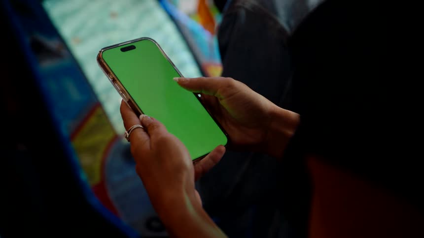 Close up of a womans hands as she uses her phone while standing close to a game machine