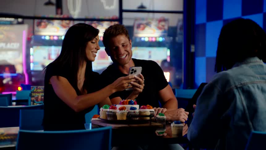 Three friends celebrate with cupcakes at a table in an arcade while clicking photo