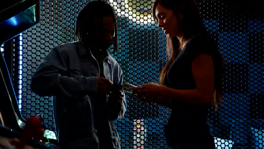Two people happily interact while exchanging tickets or cards in an arcade setting