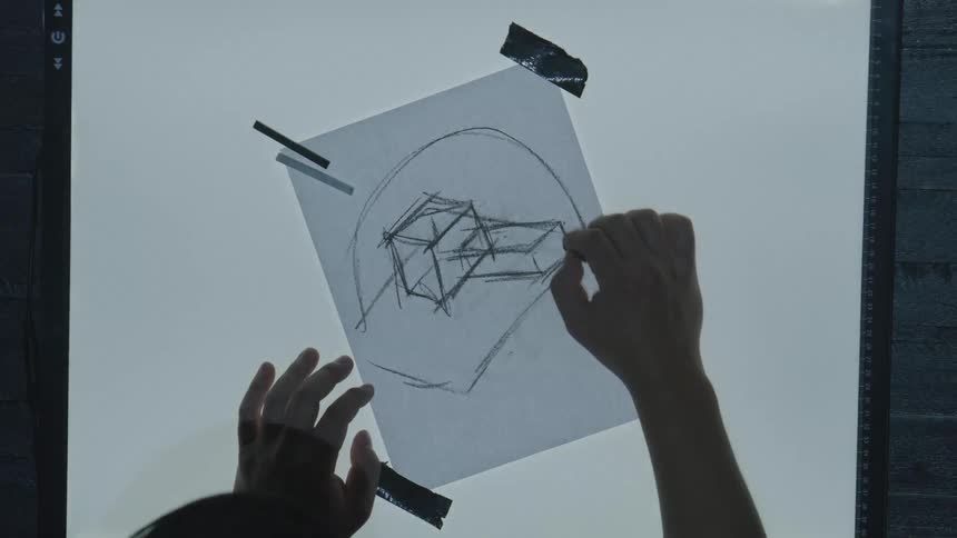 A person sketches a 3d geometric shape on tracing paper taped to a light table