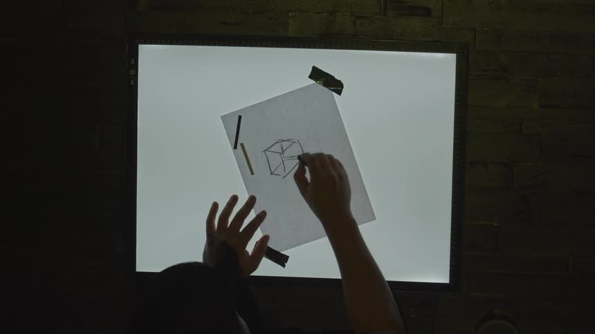 A person draws a 3d box on paper