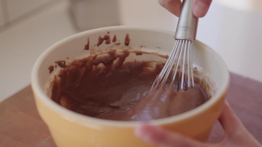 Close up of a person mixing chocolate batter in a bowl with a manual mixer