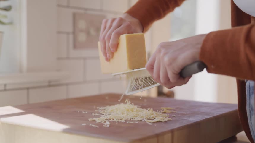 Grating parmesan cheese on a hand held grater over wood block