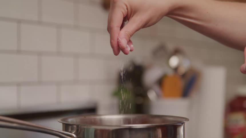 Sprinkling salt with fingertips over a metal pot in slow motion