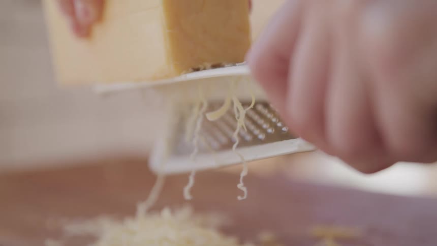 A block of cheese is being grated with a metal grater
