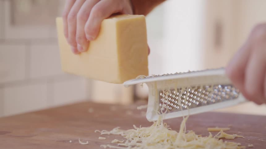 A person grates a block of cheese onto a wooden surface