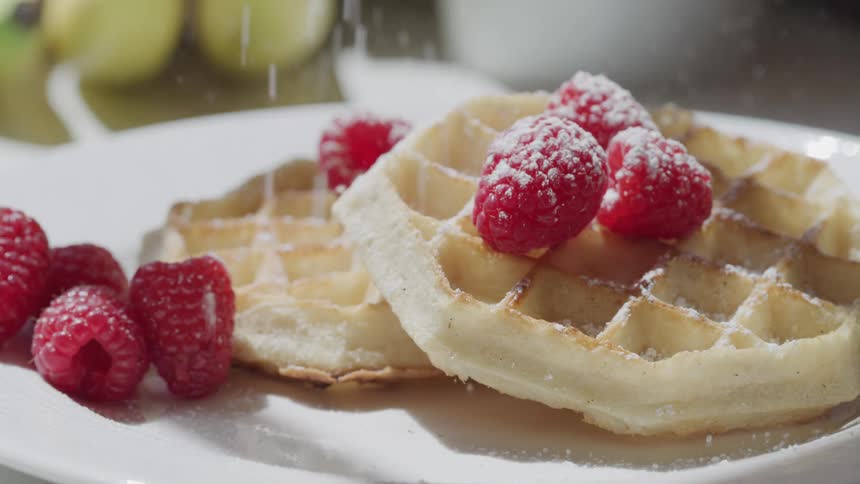 Sugar being sprinkled atop waffles with raspberries