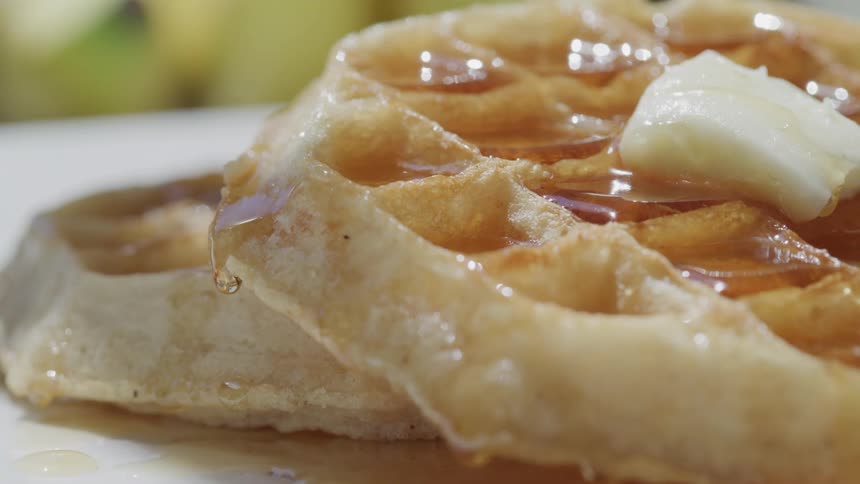 Closeup of a waffle topped with syrup and a pat of butter