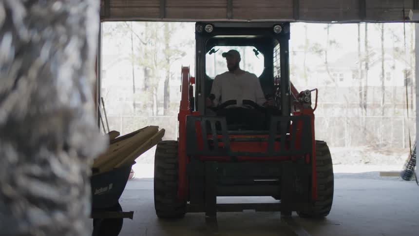 Man operates a skid steer loader inside a warehouse or garage space