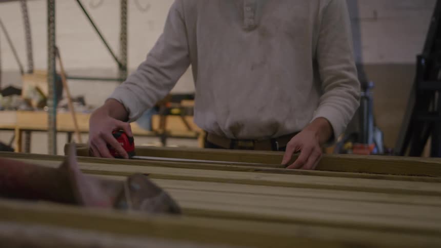 A worker measures wood with a tape measure focusing on the task in a workshop setting