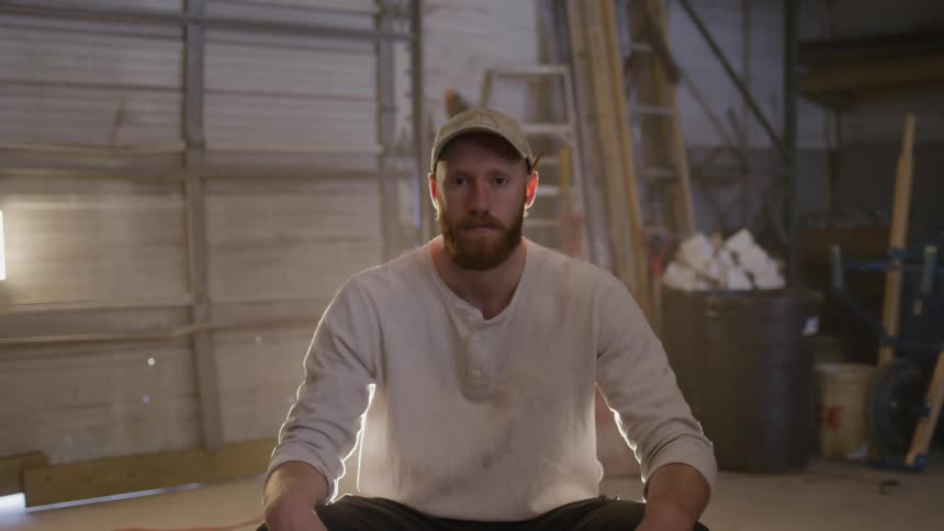 Man sits in a workshop facing the camera