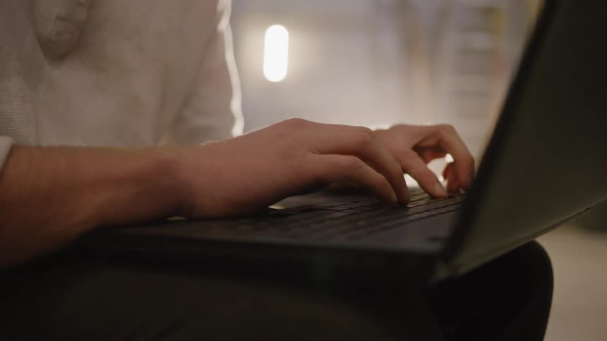 Close up of a man typing on a laptop computer placed on his laps while sitting