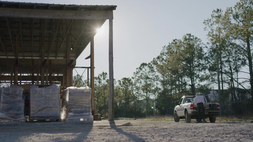 Man loads wooden planks into a pickup by a warehouse