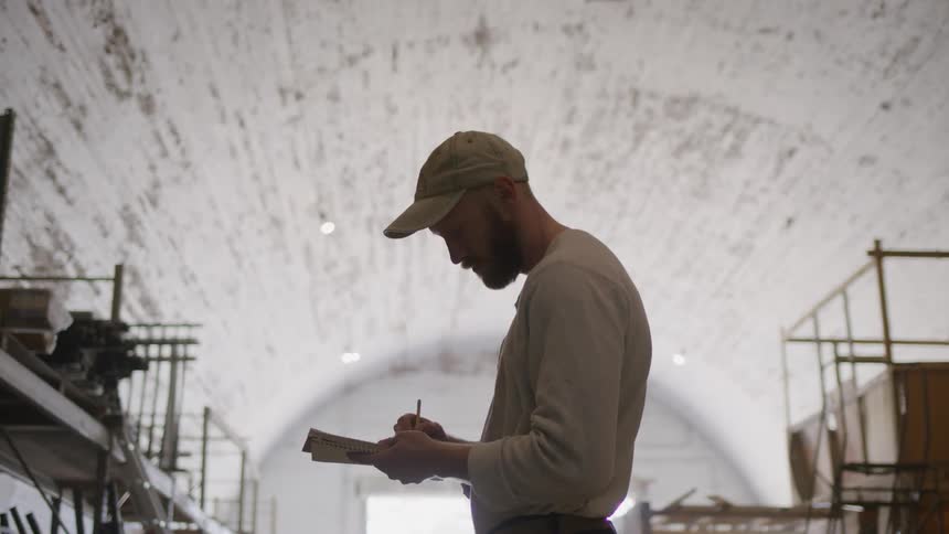 A man wearing a hat takes inventory of warehouse stocks