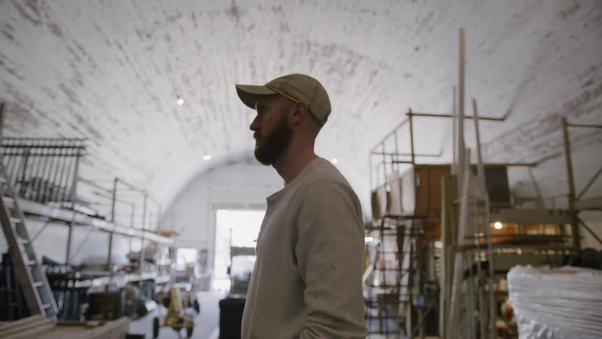 A man wearing a hat takes inventory records inside a warehouse