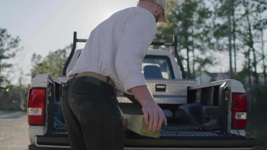 Male carpenter places a wood plank in the back of his truck and sits at the back of the truck during daytime