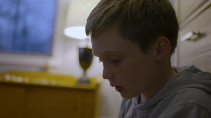 The face of a little boy looking down in an indoor setting with a window in the background