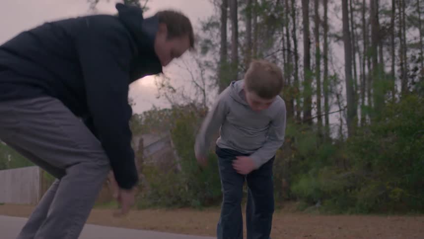 Boy falls as a young man tries teaching him a skateboard stunt on a road during daytime