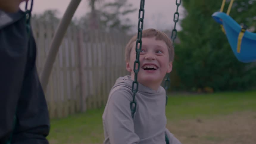 Happy child laughing with his dad as they swing on a swingset in the backyard