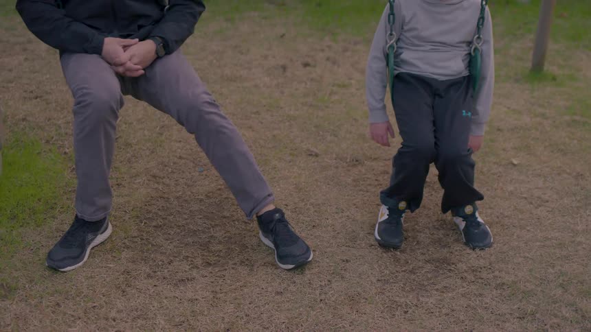 A father and son sit on swings in the park