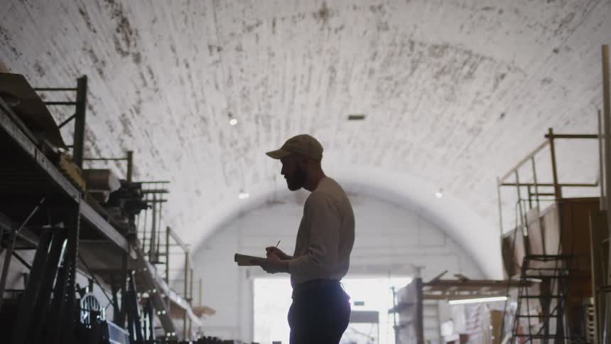 A man wearing a hat takes inventory of warehouse stocks