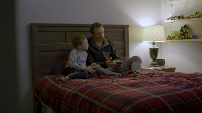A father reads a bedtime story to his son in a cozy softly lit bedroom