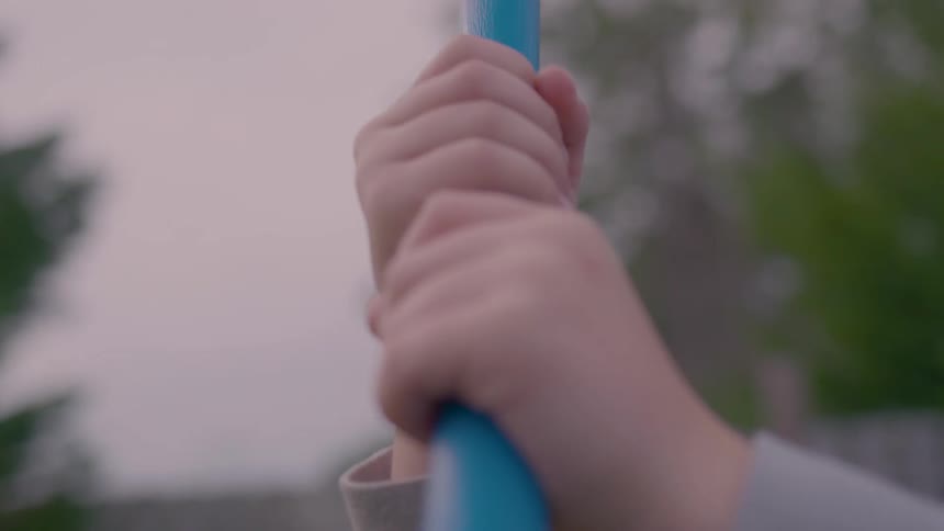 Hands grips a blue pole with tall trees and overcast day in the background