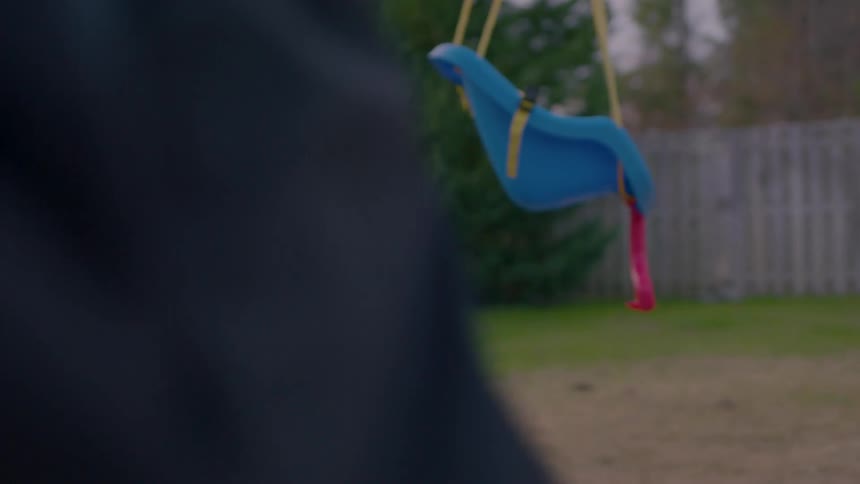 A young boy sits on a swing and looks up attentively in a backyard setting