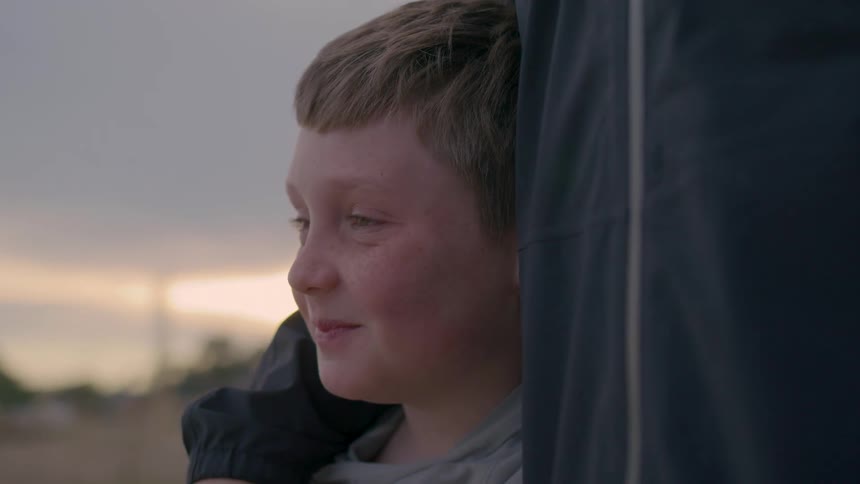 Close up of boy laughing while standing with a young man outdoors at sunset
