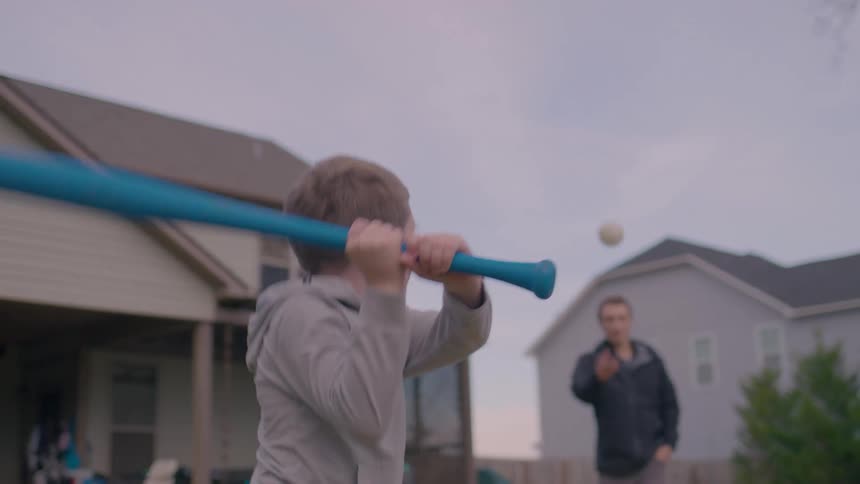 A boy prepares to swing a bat as his father gets ready to pitch in a suburban backyard