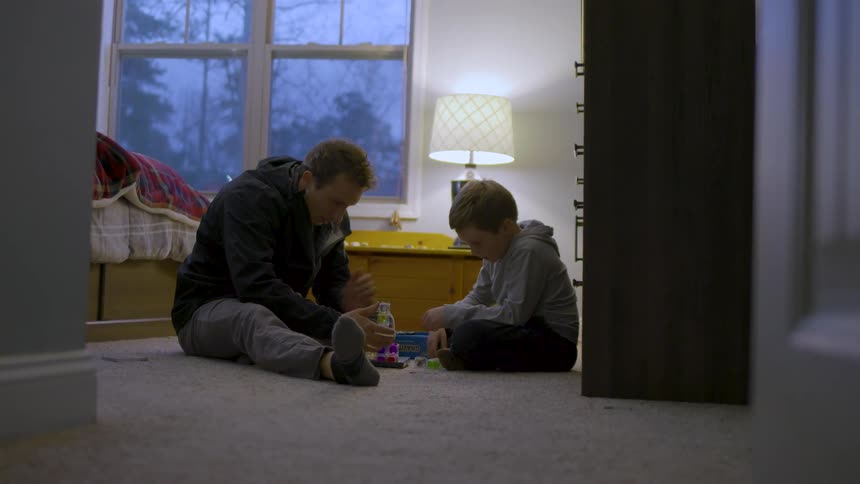 Father and son sit on the bedroom floor focused on building toys together