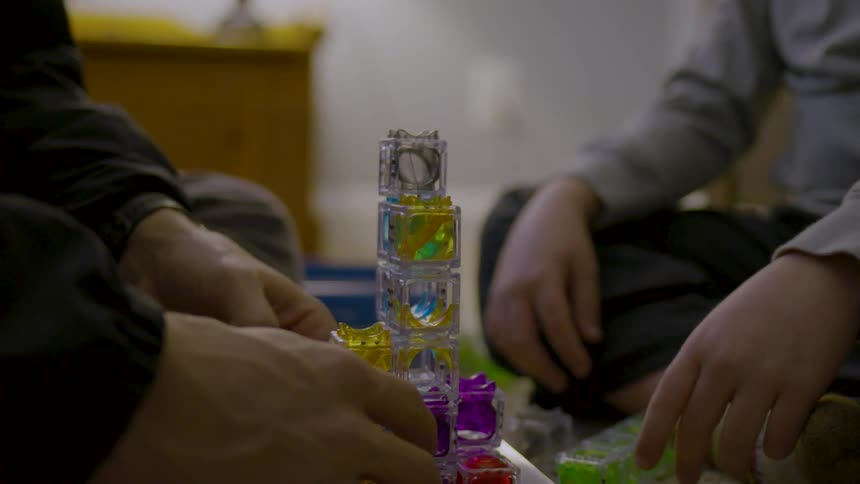A father and son sit on the floor arranging a block maze together