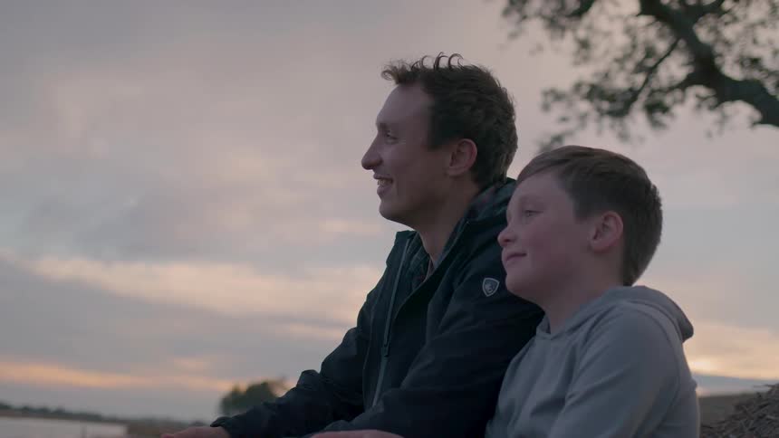 A father and son share a warm smiling moment outdoors at sunset