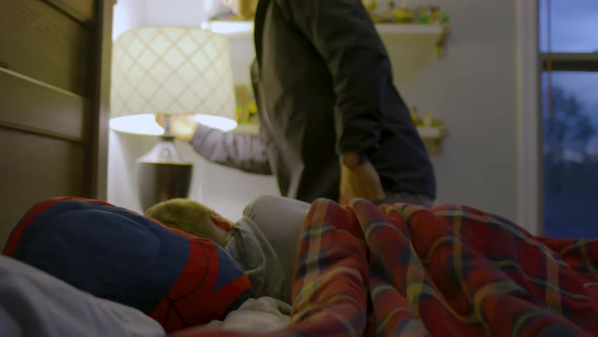 A father kisses his son goodnight while tucking him into bed