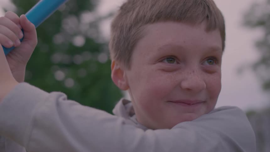A smiling young boy eagerly holds a blue baseball bat anticipating the pitch