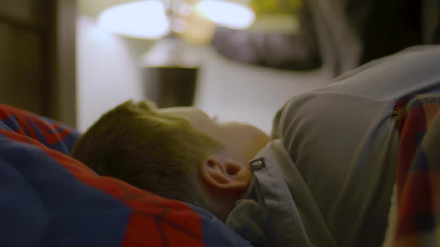 Young man kisses his younger brother to sleep and puts off the room lamp at nighttime