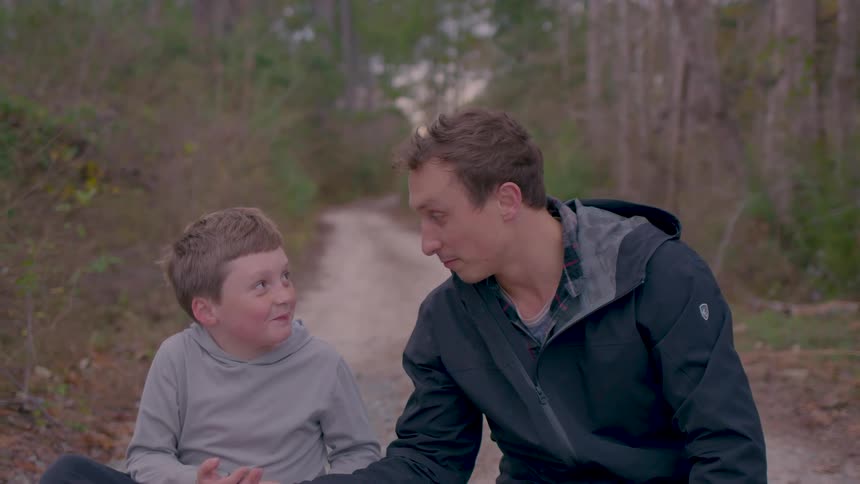 Father and son smile and talk together while sitting on a forest path