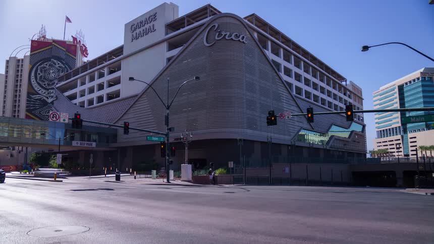 A corner building with writing on the top and an intersection in front with several cars passing by in downtown Las Vegas