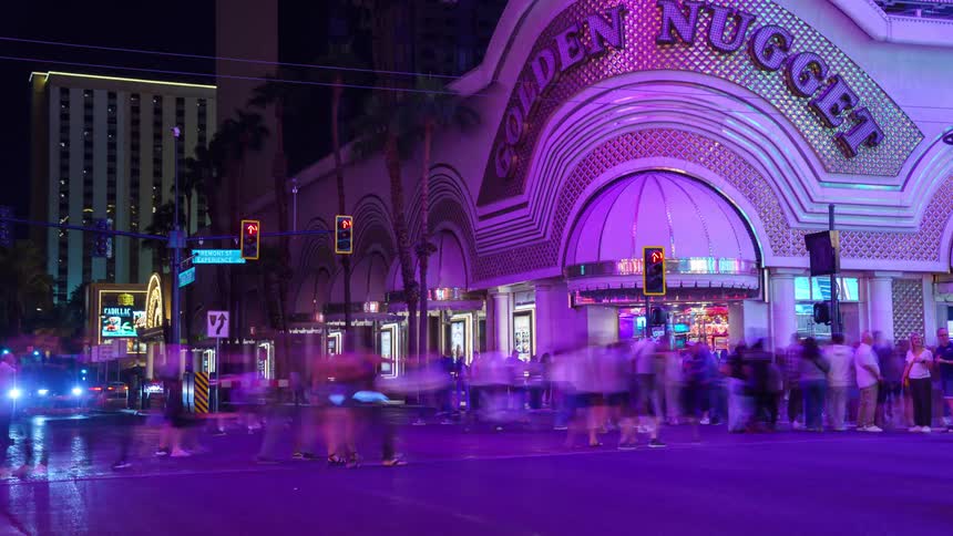 A tourist building at the Fremont Street Experience in downtown Las Vegas with many people passing in front at night and with some cars stopping at the traffic lights