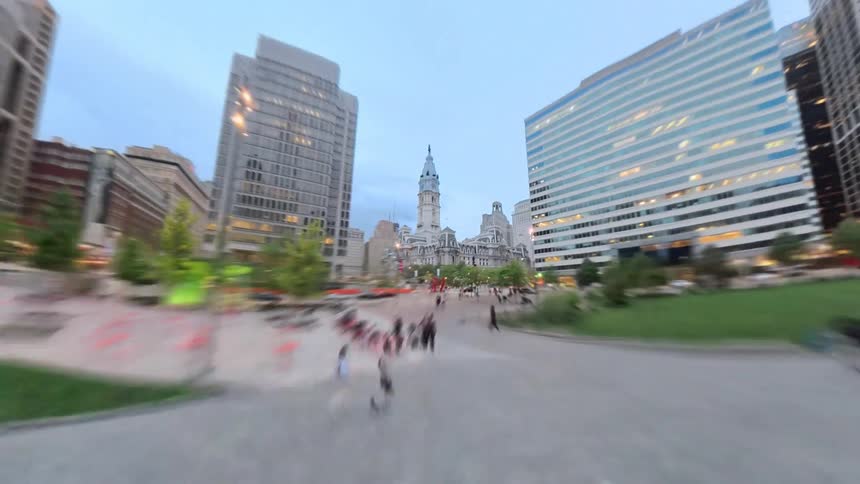 A Philadelphia cityscape view showcasing a network of streets and roads with a fountain park at the center as people walk and cars move along